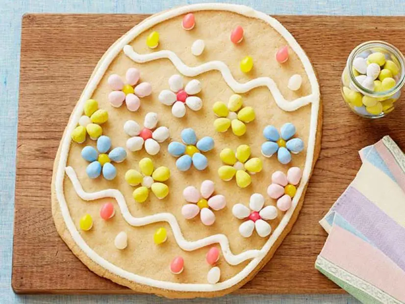 Large oval sugar cookie decorated with white icing drizzle and colorful candy eggs arranged in festive patterns